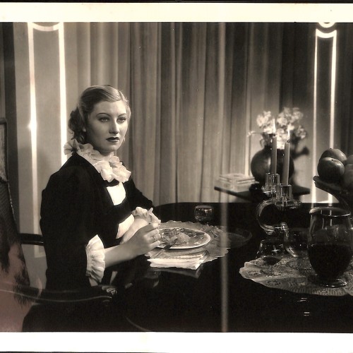 Fotografía original de producción: Escena dramática interior con actriz principal en mesa de comedor