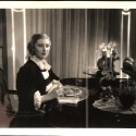 Fotografía original de producción: Escena dramática interior con actriz principal en mesa de comedor