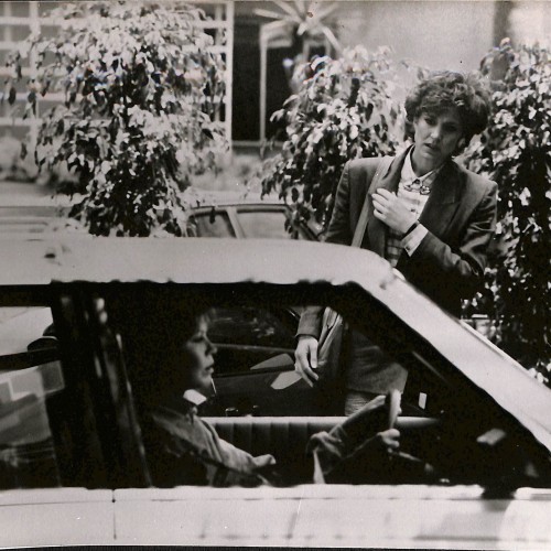 Fotografía de rodaje en blanco y negro mostrando a dos mujeres junto a un coche, década de 1980
