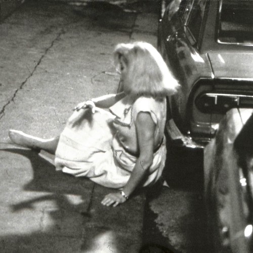 Fotografía en blanco y negro de mujer caída junto a un coche