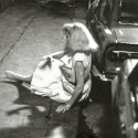 Fotografía en blanco y negro de mujer caída junto a un coche