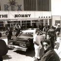 Fotografía en blanco y negro, escena exterior frente al cine REX con patrulla de policía y multitud