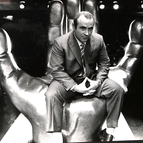 Fotografía en blanco y negro de hombre sentado sobre escultura en forma de mano gigante