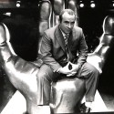 Fotografía en blanco y negro de hombre sentado sobre escultura en forma de mano gigante