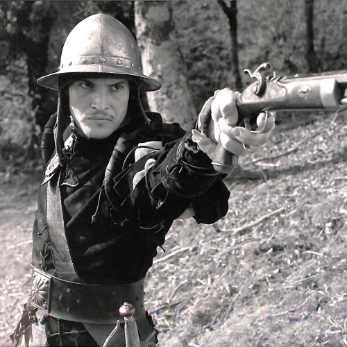 Fotografía en blanco y negro, escena de época con personaje empuñando arma de fuego