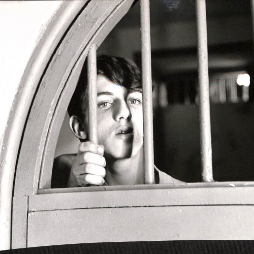 Fotografía en blanco y negro de un joven tras unos barrotes