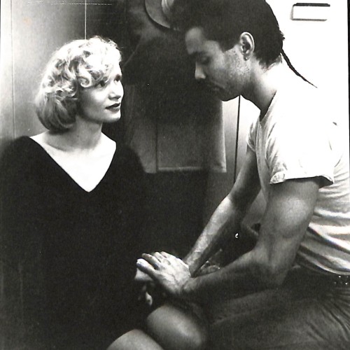 Fotografía en blanco y negro, escena con dos personajes y un tercero al fondo