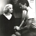 Fotografía en blanco y negro, escena con dos personajes y un tercero al fondo